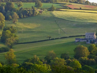 Sun rising over a farmhouse and field 