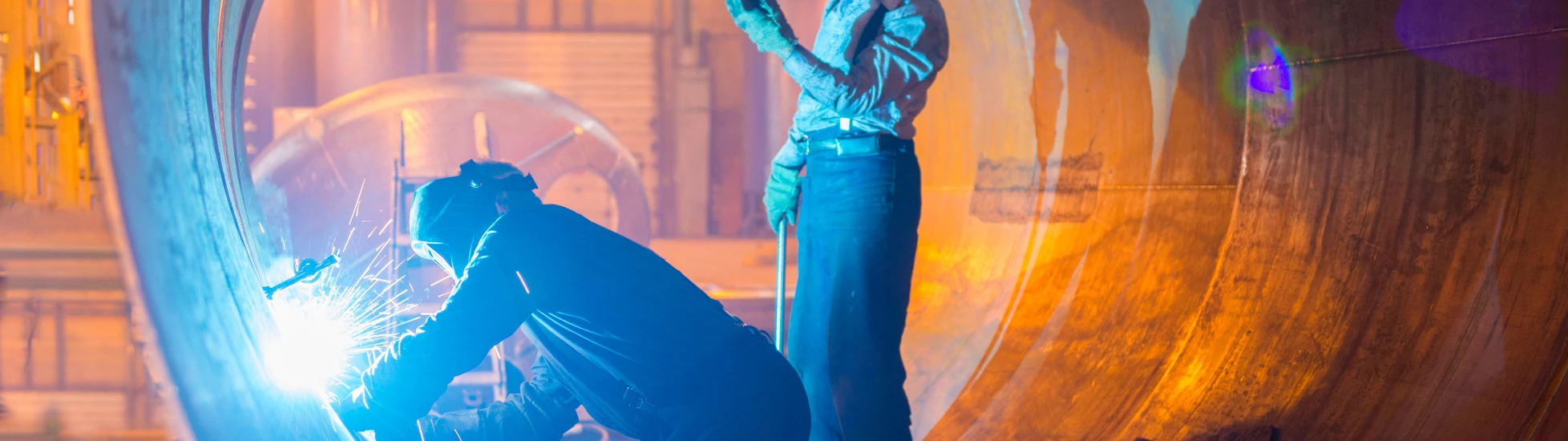 Two male welders working on metal pipe