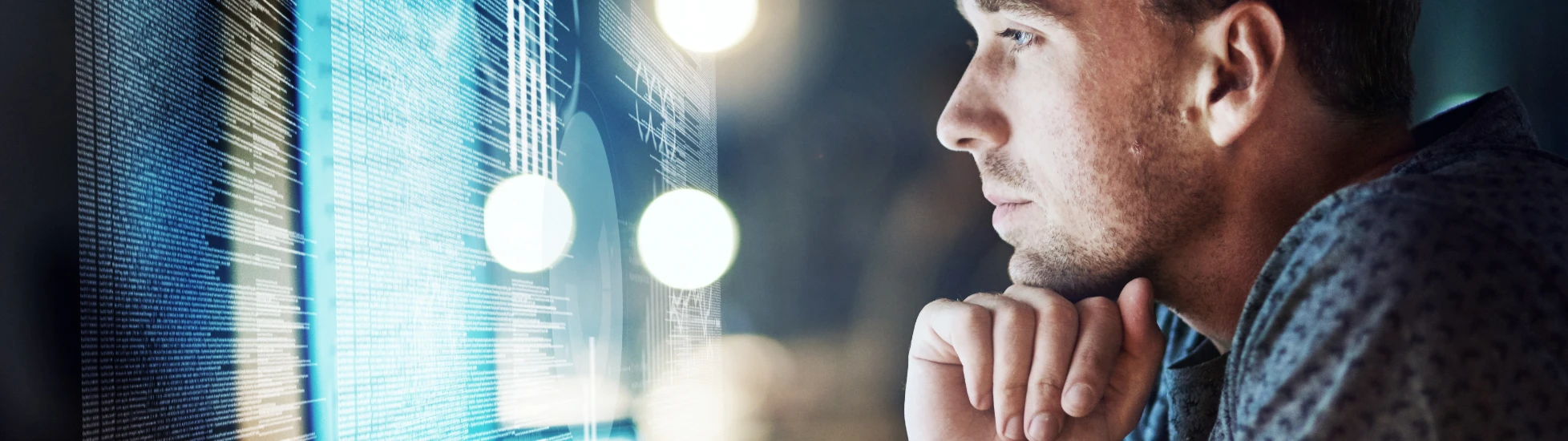 Man looking at computer code on a screen with blue lighting