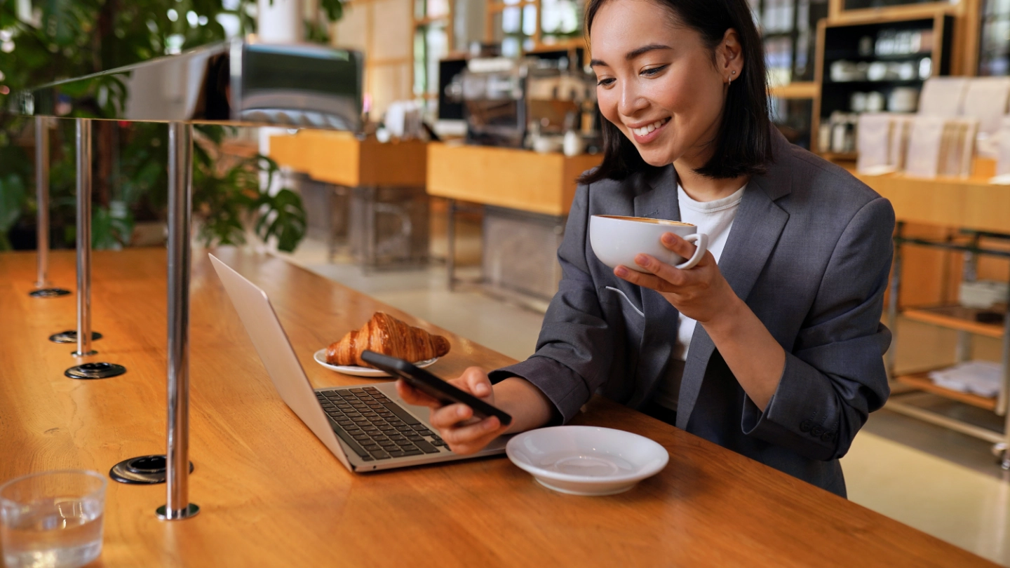 Young Asian business woman drinking coffee using smartphone in cafe