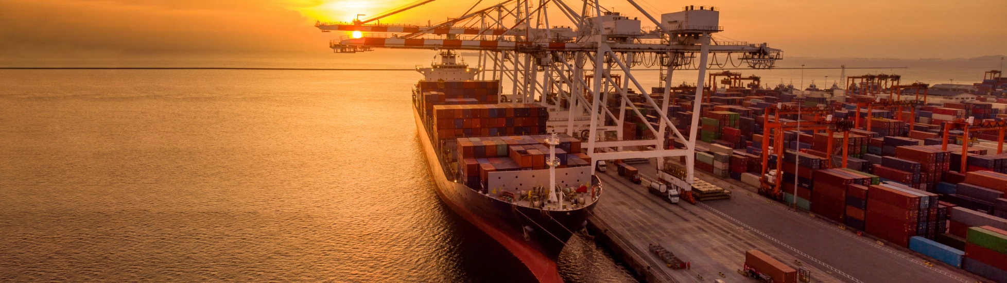 Crane loading container onto container ship at sunset