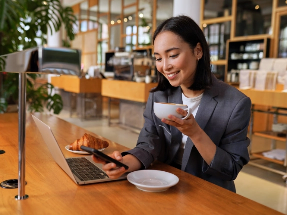 Young Asian business woman drinking coffee using smartphone in cafe