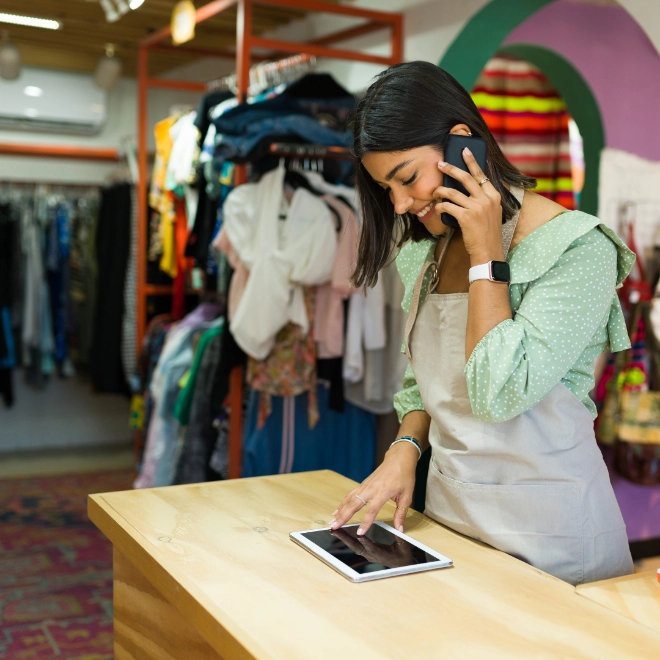 Woman working behind a shop counter on the phone and looking at a tablet