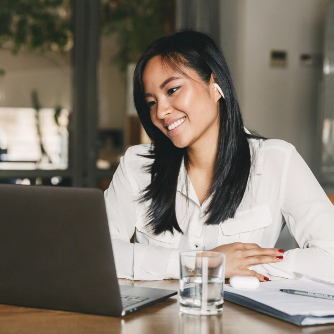 Woman with glass of water working from a laptop with a smile on her face